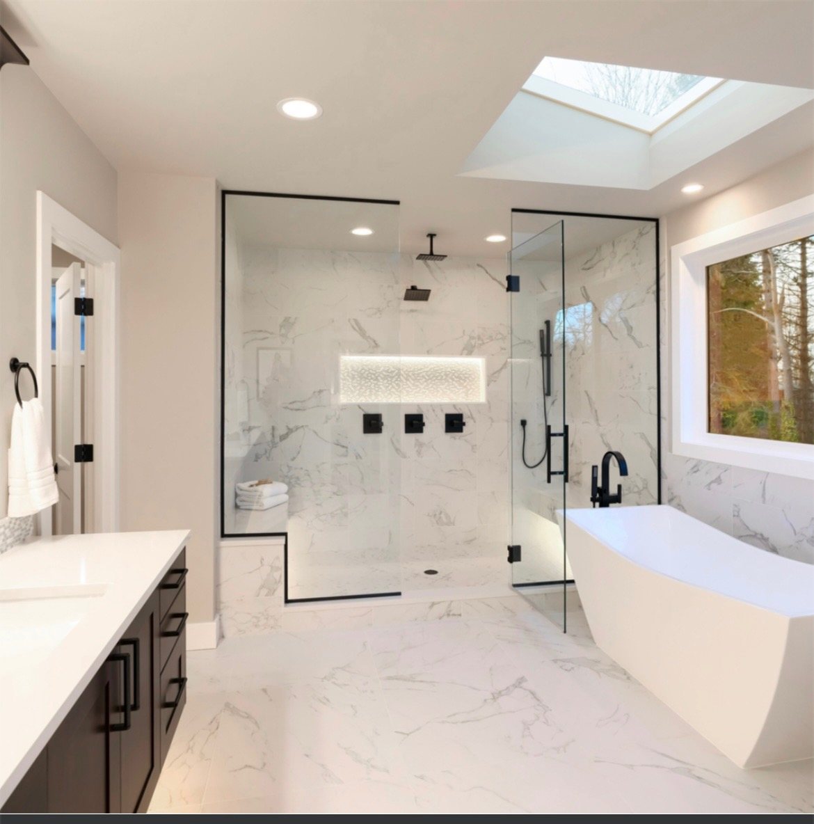 Ultra-modern marble bathroom with skylight, glass walk-in shower, and freestanding tub
