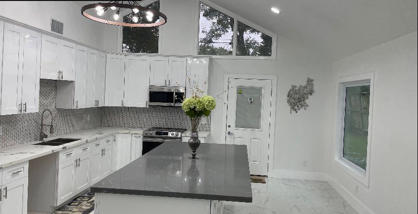 Renovated kitchen with white cabinets, gray waterfall island, and vaulted ceiling